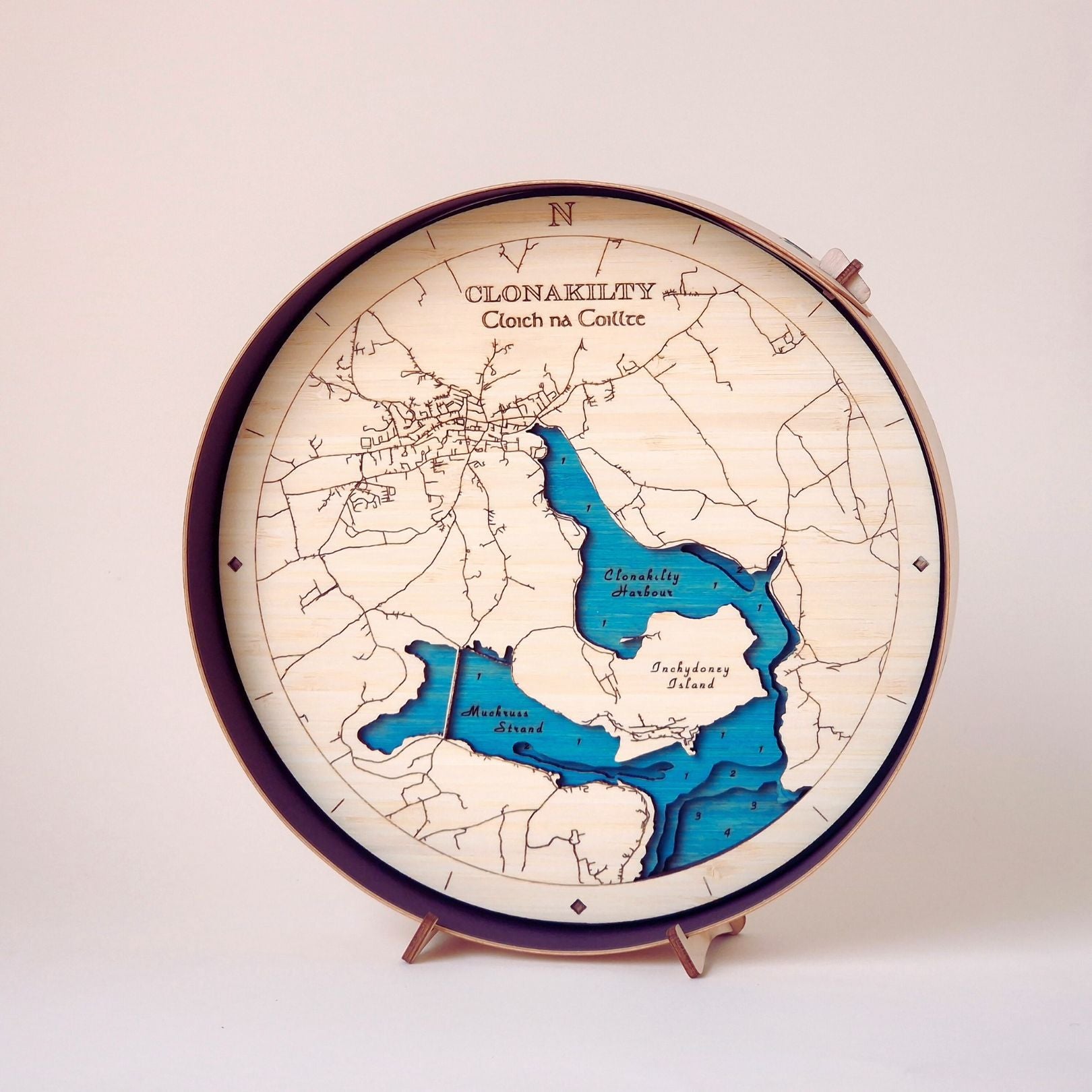 Round wooden 3d handcrafted map art of Clonakilty and Inchydoney in a black frame on a wooden stand