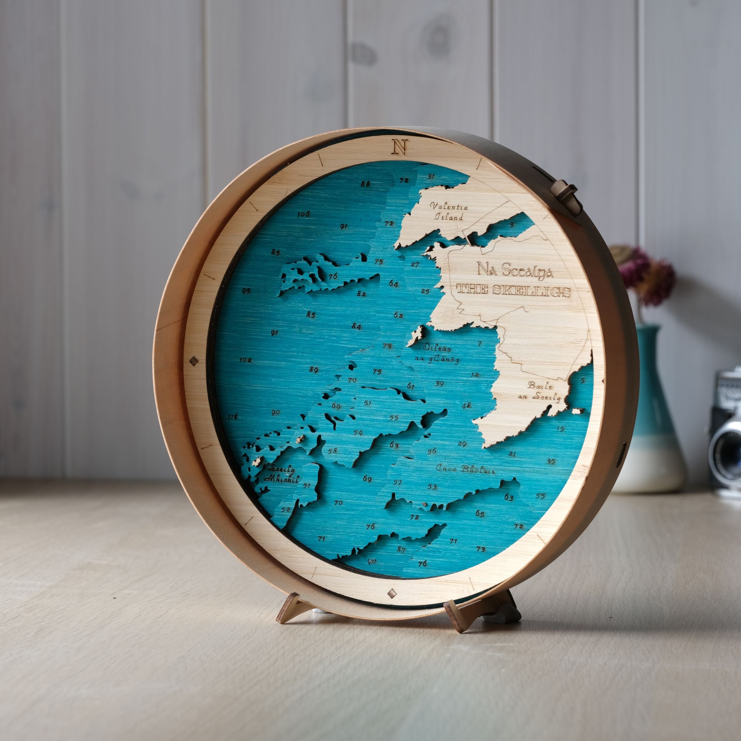 The Skelligs round wooden map in a natural frame, showing Skellig Michael and Little Skellig, styled on a wall shelf in a bright, modern coastal interior.