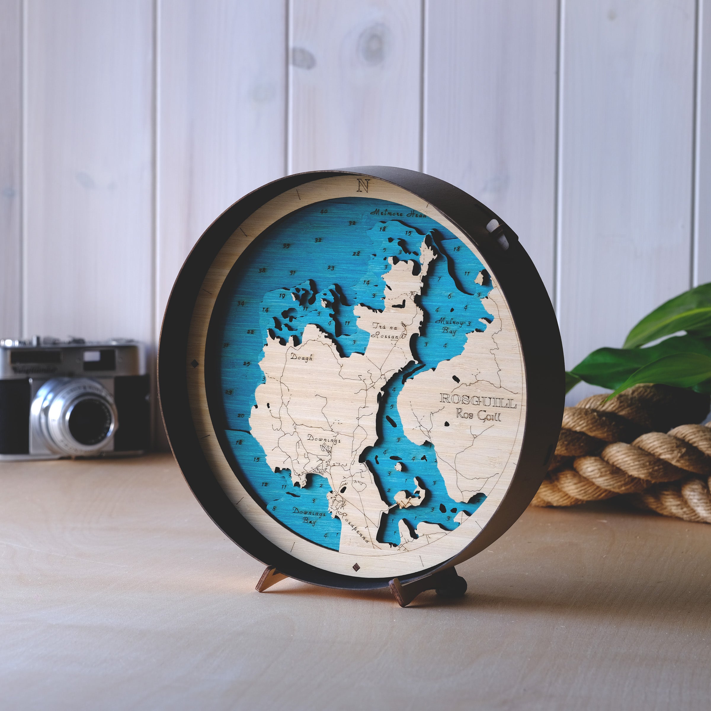 Outcrop’s handcrafted round 3D wooden map of Rosguill Peninsula, County Donegal – precision-cut layers of sustainable bamboo plywood in a minimalist natural wood frame, featuring a signature Atlantic blue sea and a black frame