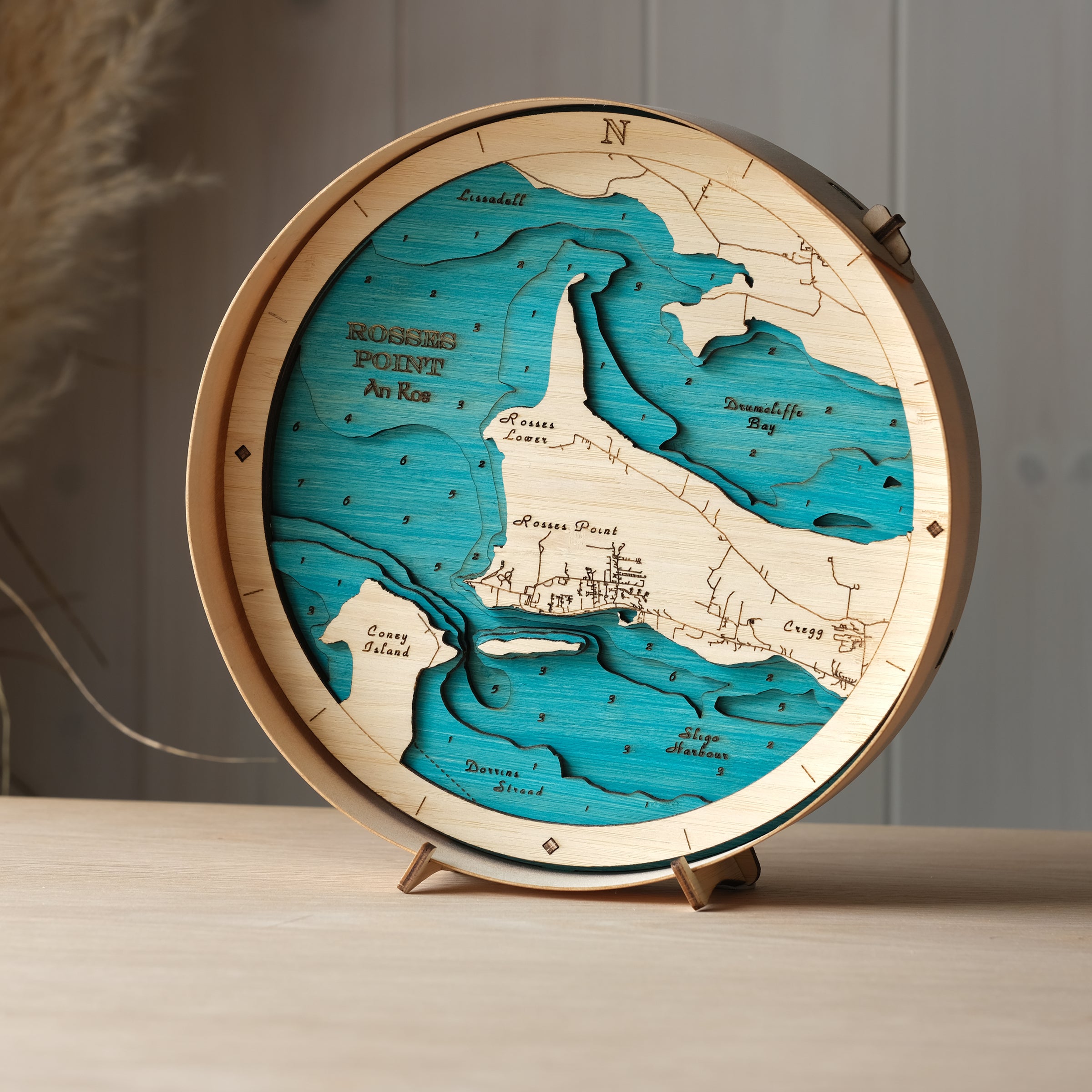 Round 3D wooden map of Rosses Point in natural birch frame, displayed on a shelf with stand, handcrafted by Outcrop