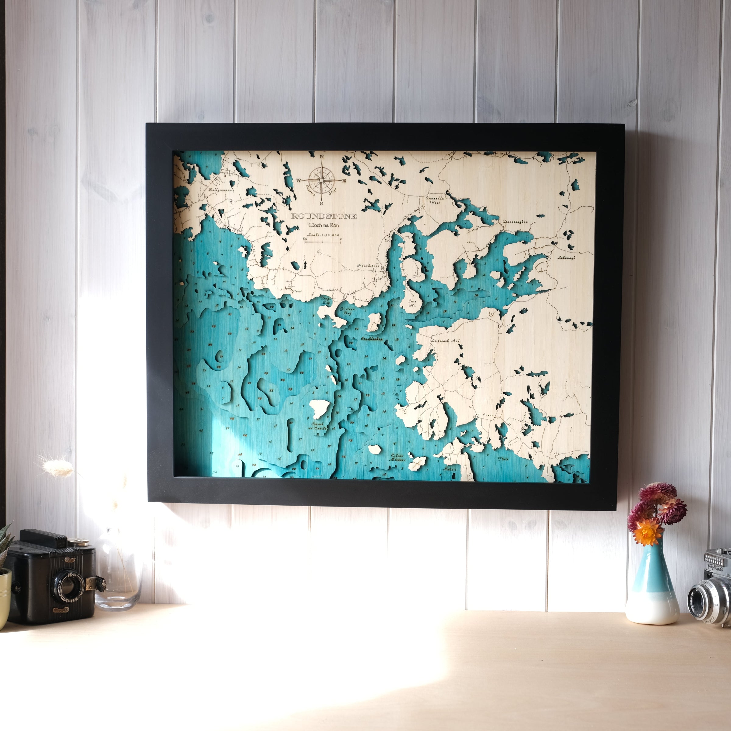 Framed topographic map of a coastal area on a wall with decorative items below.