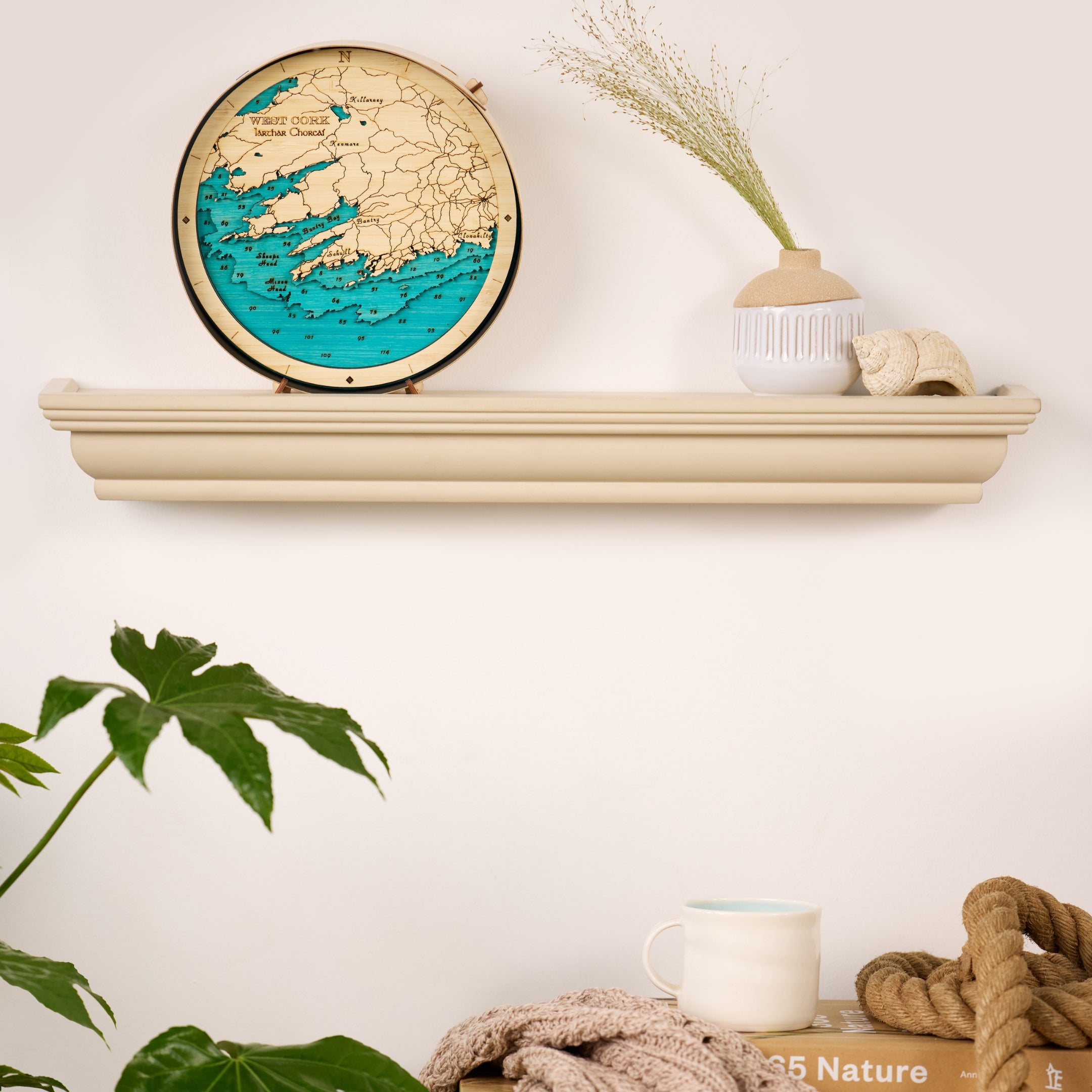West Cork round wooden 3d map in a black frame, styled on a wall shelf in a bright, modern sitting room with high-end minimalist decor.