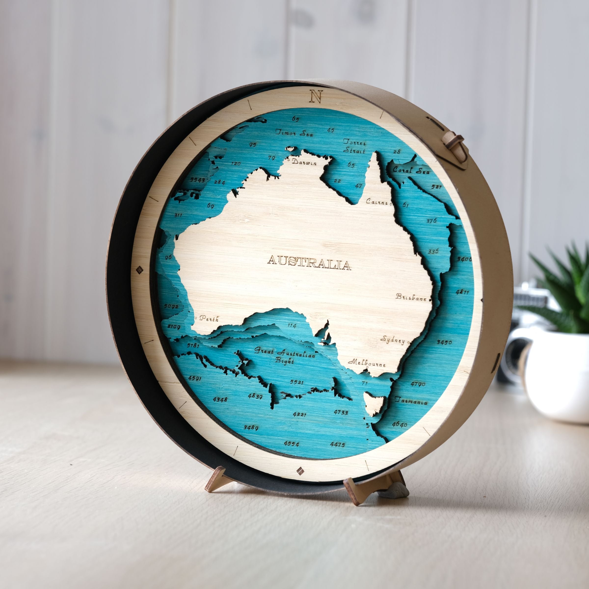 Wooden map of Australia on a stand with a black round wooden frame and a blue stain on the sea color scheme.
