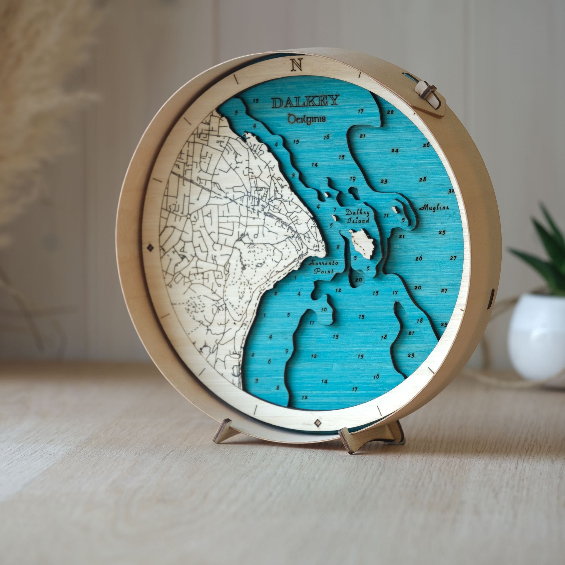 Handcrafted wooden map of Dalkey in a natural wood frame, styled on an oak table with a pot plant behind for a cosy setting.