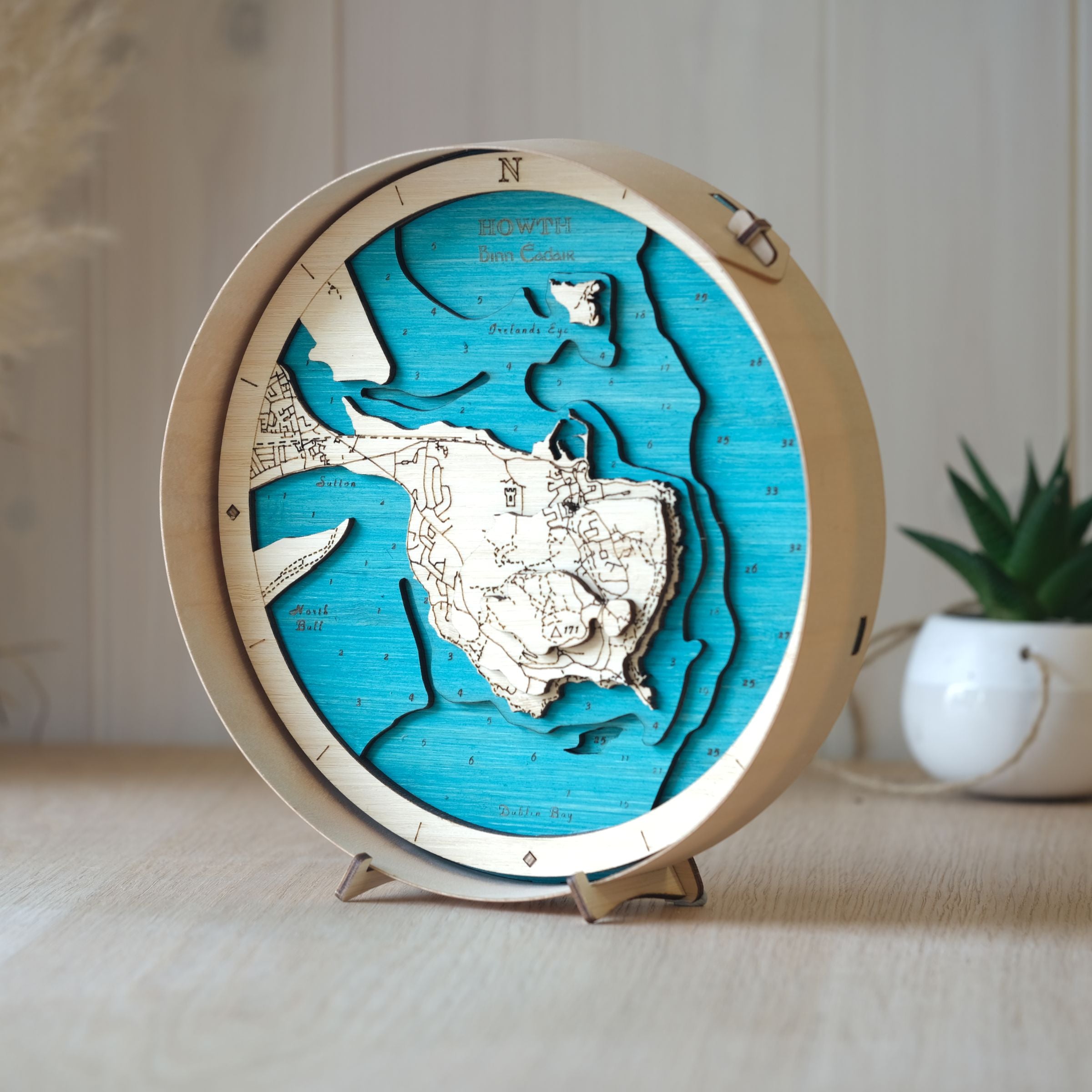 Beautifully layered wooden map of Howth, framed in natural wood, styled on an oak table with a pot plant in the background.