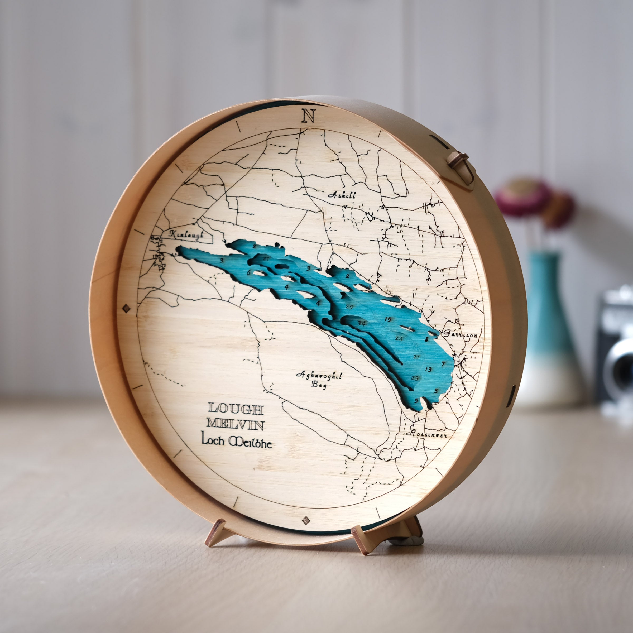 Lough Melvin round wooden map in a natural frame, styled on a wall shelf in a bright, modern interior with clean Irish countryside decor.