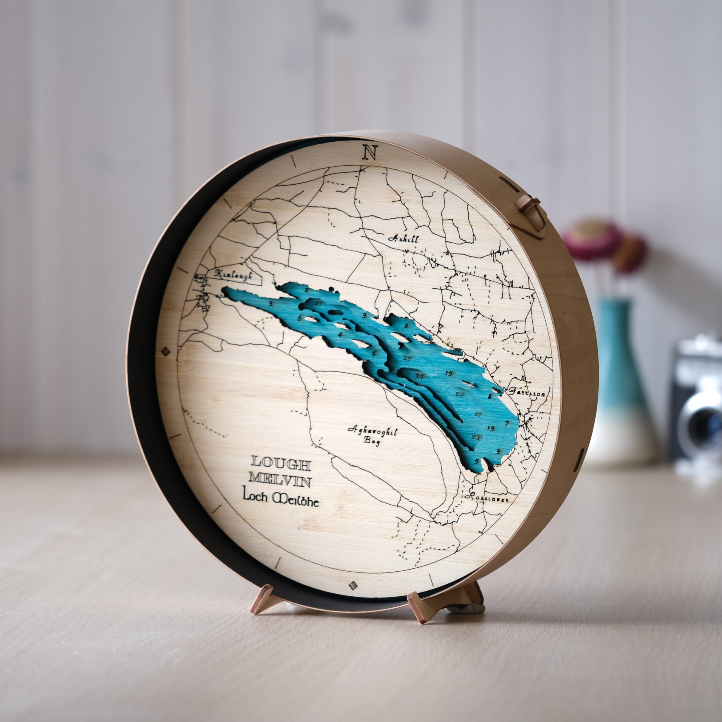 Lough Melvin round wooden map in a black frame, styled on a wall bench in a bright, modern interior with clean Irish countryside decor.