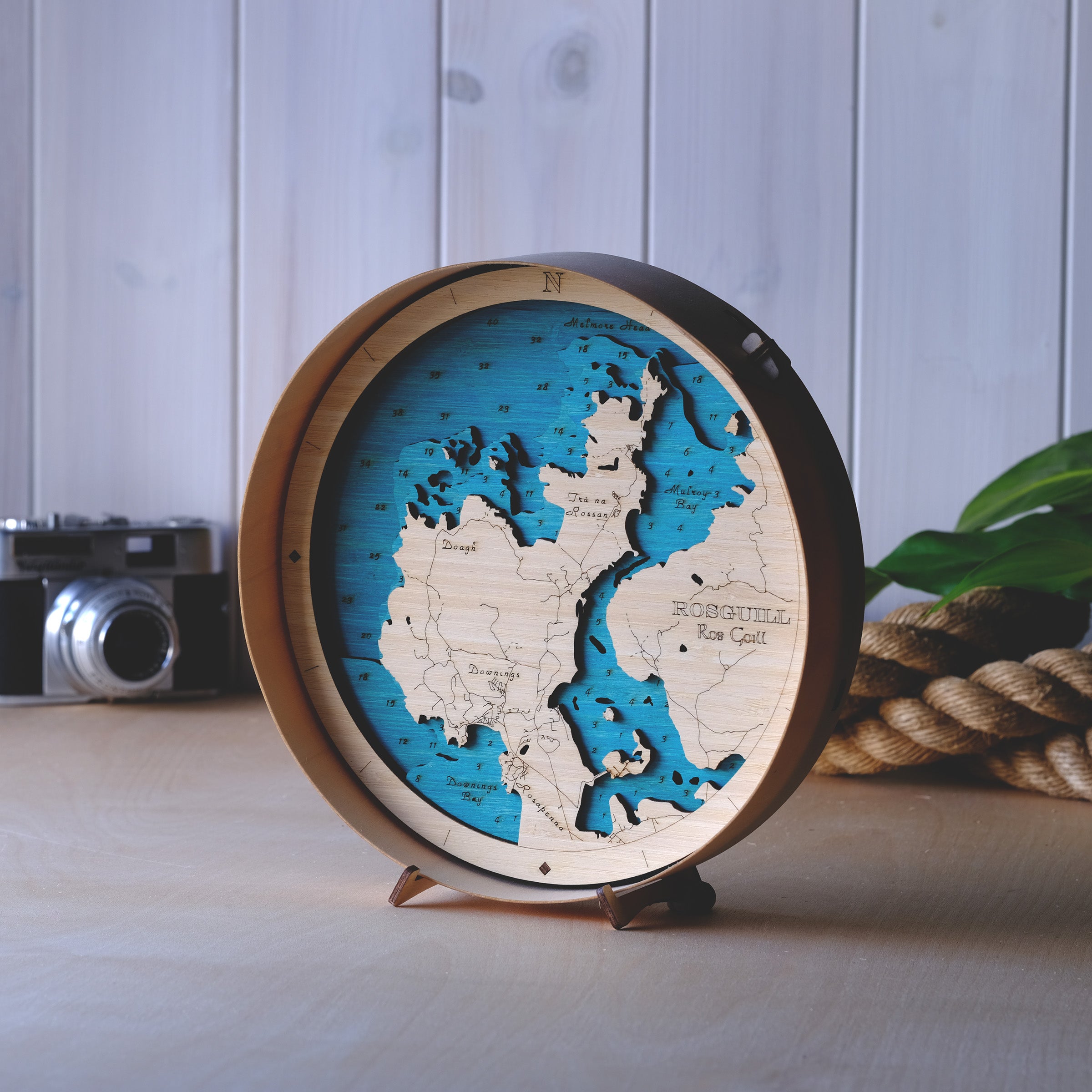Outcrop’s handcrafted round 3D wooden map of Rosguill Peninsula, County Donegal – precision-cut layers of sustainable bamboo plywood in a minimalist natural wood frame, featuring a signature Atlantic blue sea and a natural birch frame