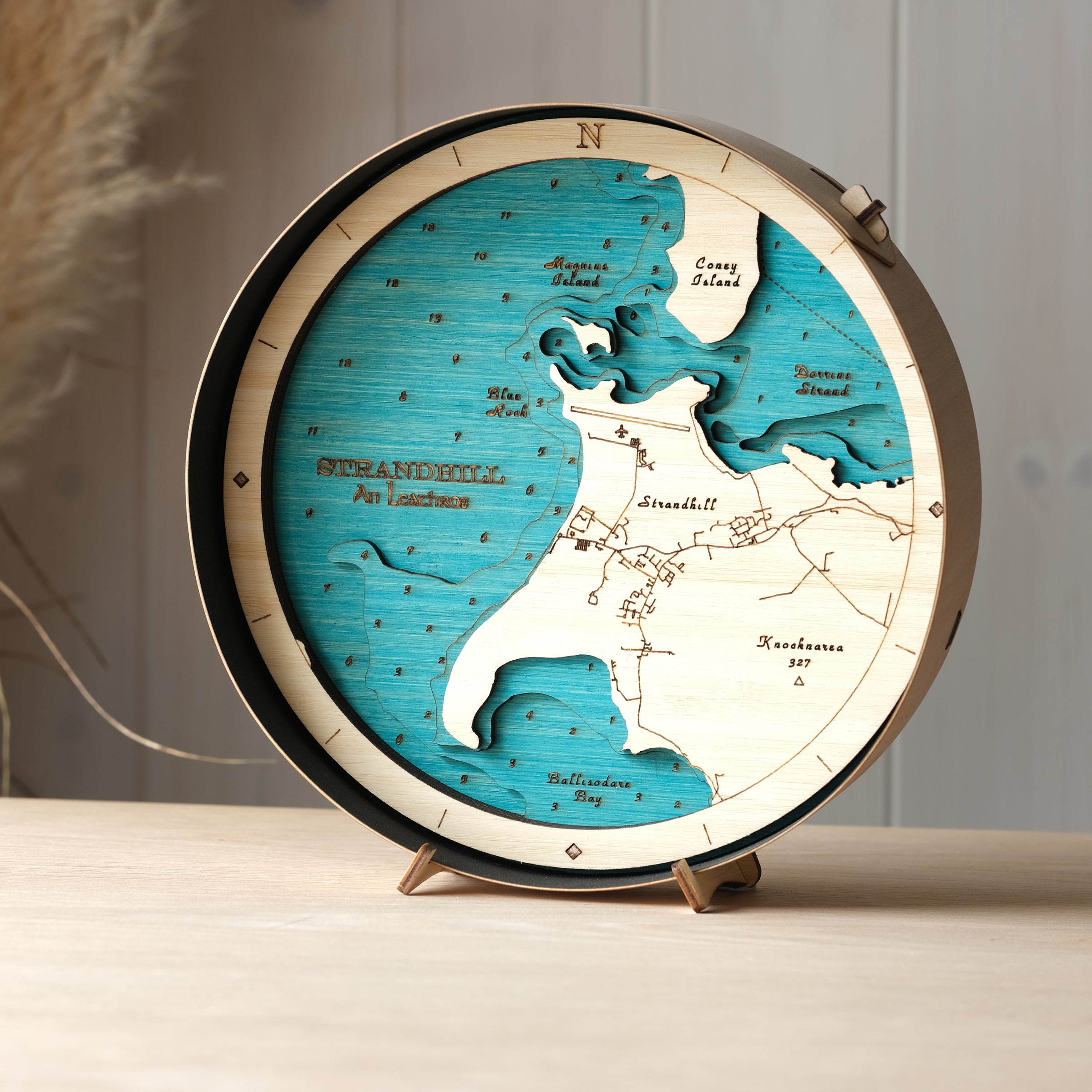 Round 3D wooden map of Strandhill in black birch frame, displayed on a shelf with stand, handcrafted by Outcrop