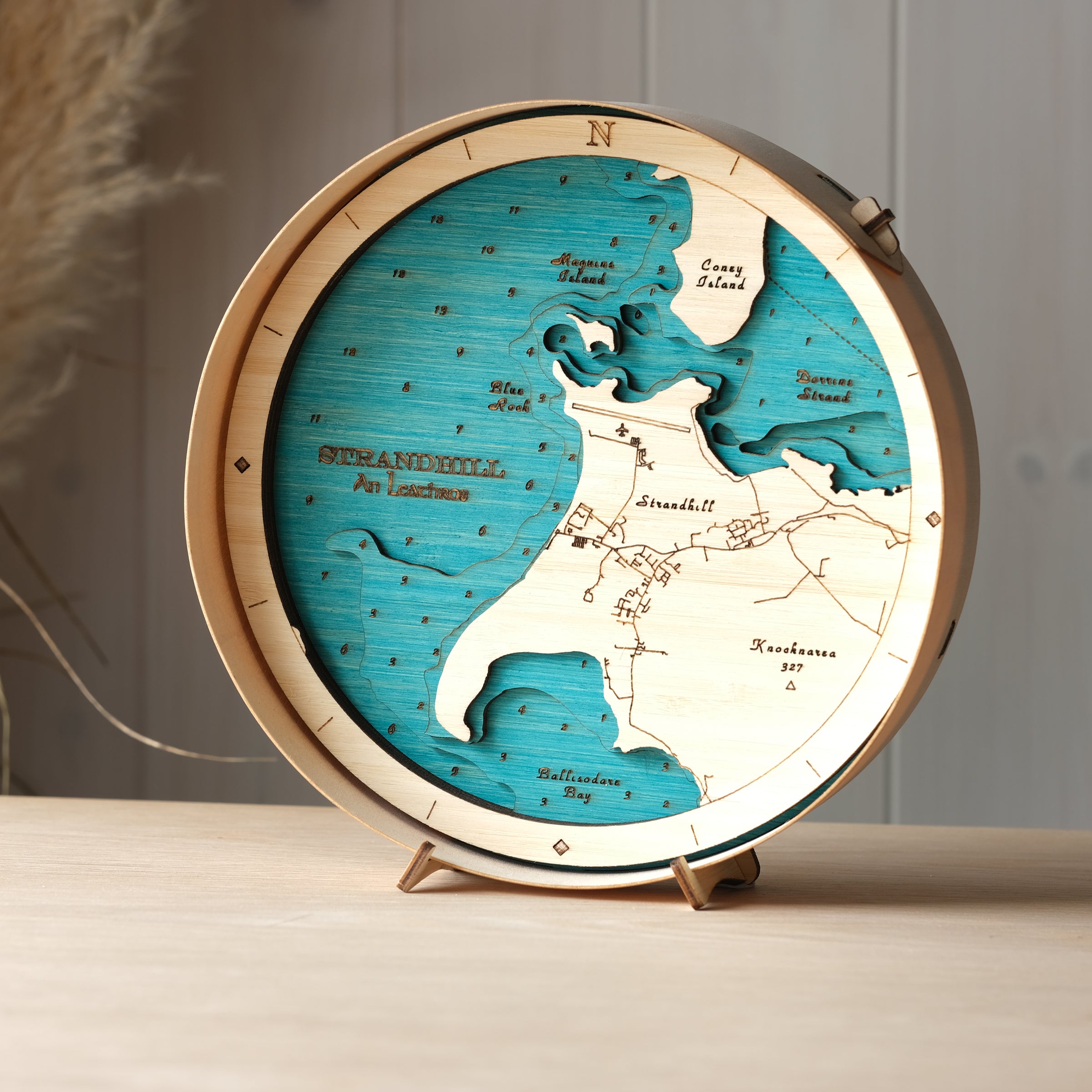 Round 3D wooden map of Strandhill in natural birch frame, displayed on a shelf with stand, handcrafted by Outcrop
